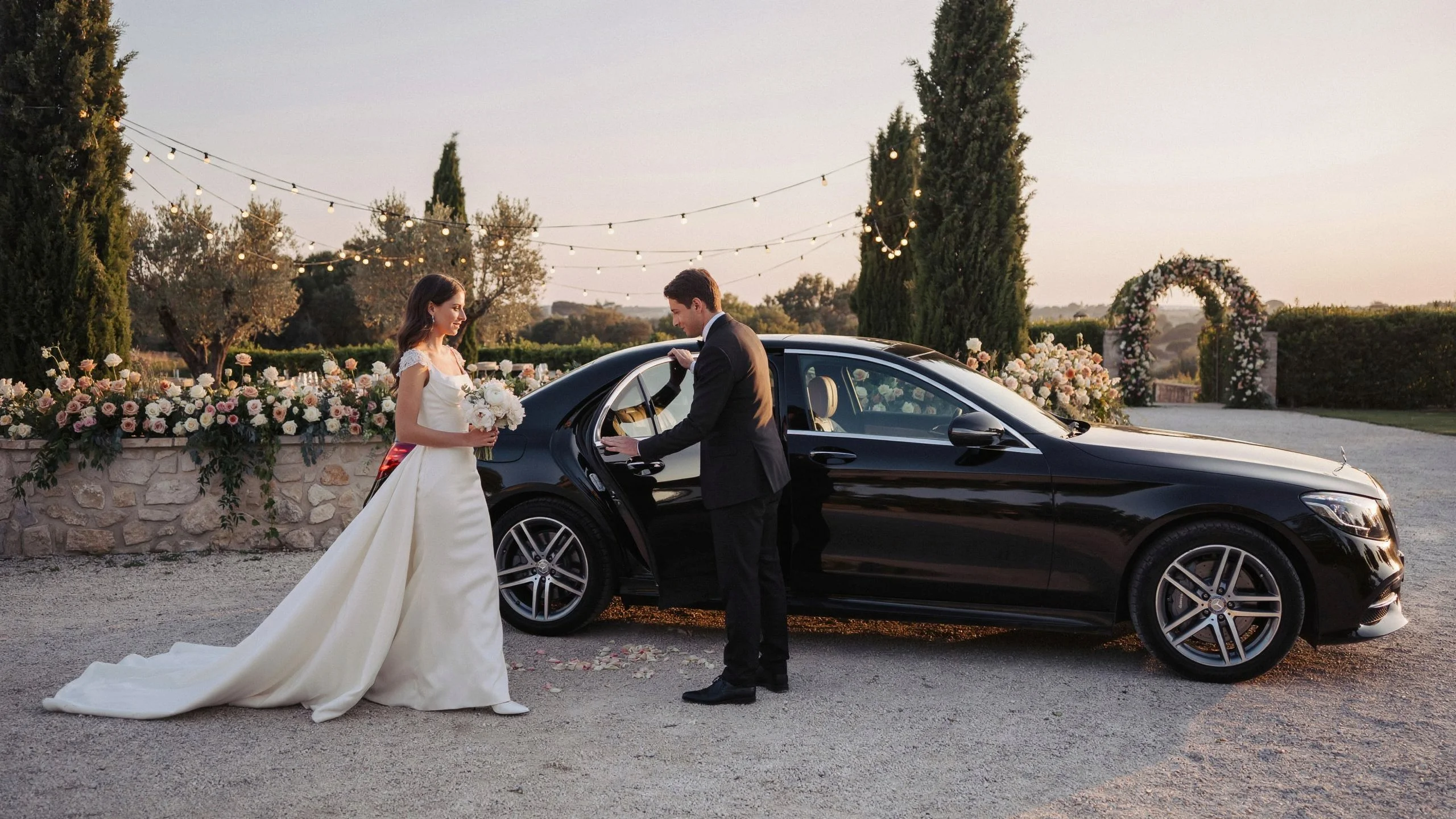 Groom opening door of black luxury sedan for bride at wedding venue