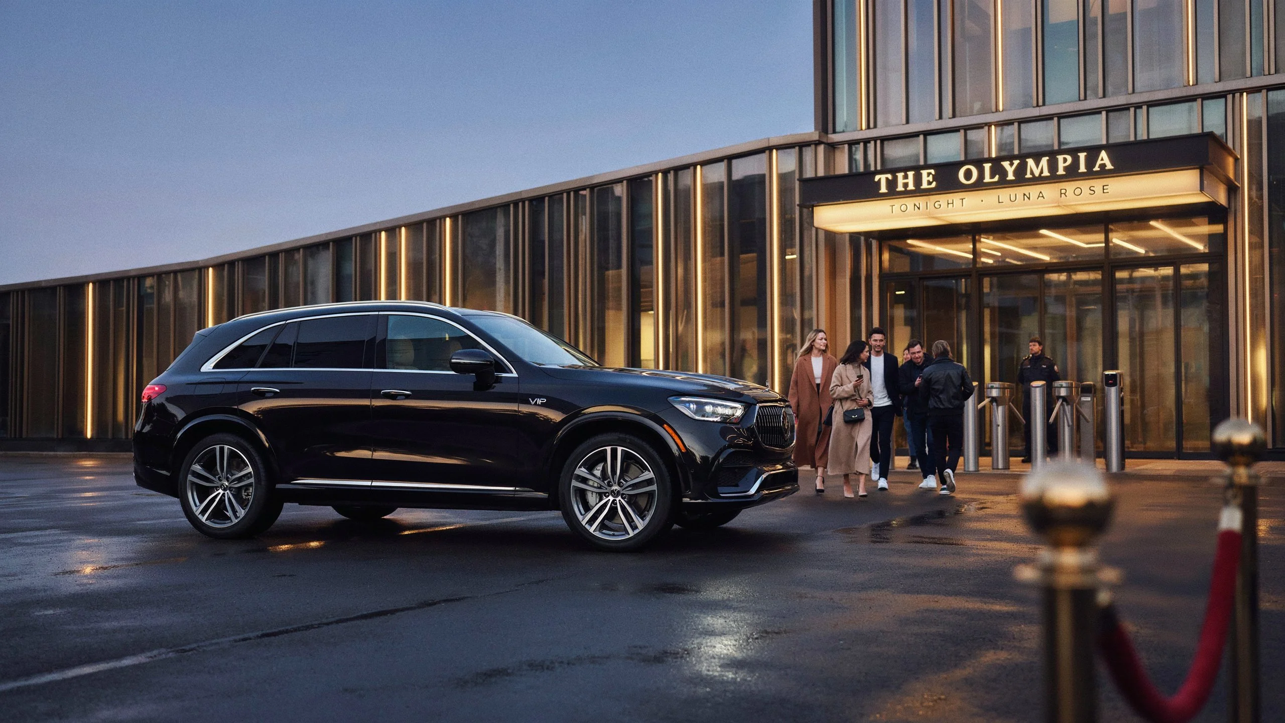 Black luxury SUV near a valet stand outside a concert venue as guests arrive in the evening